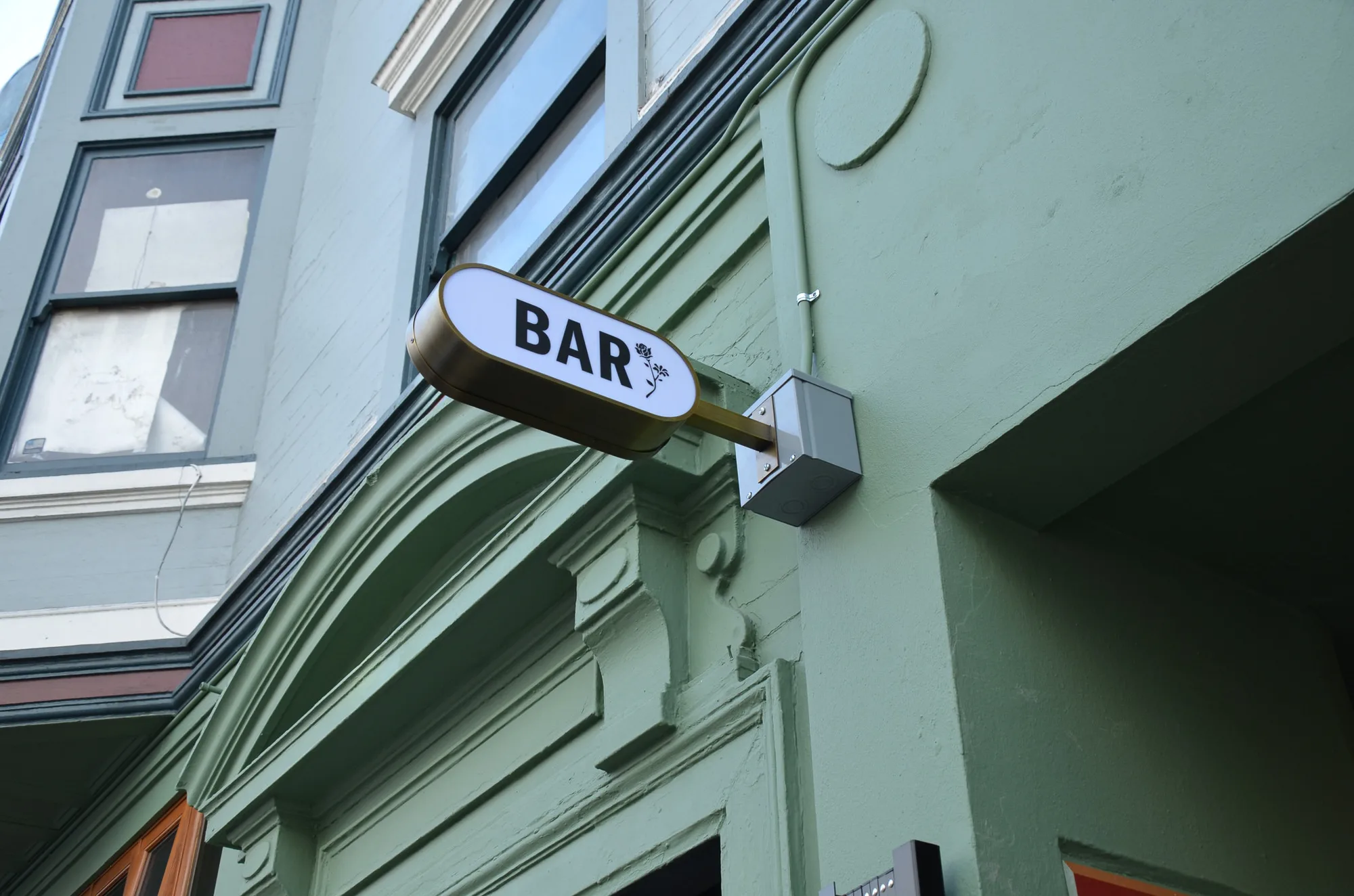 A rounded blade sign reading BAR mounted on a sage-green facade.