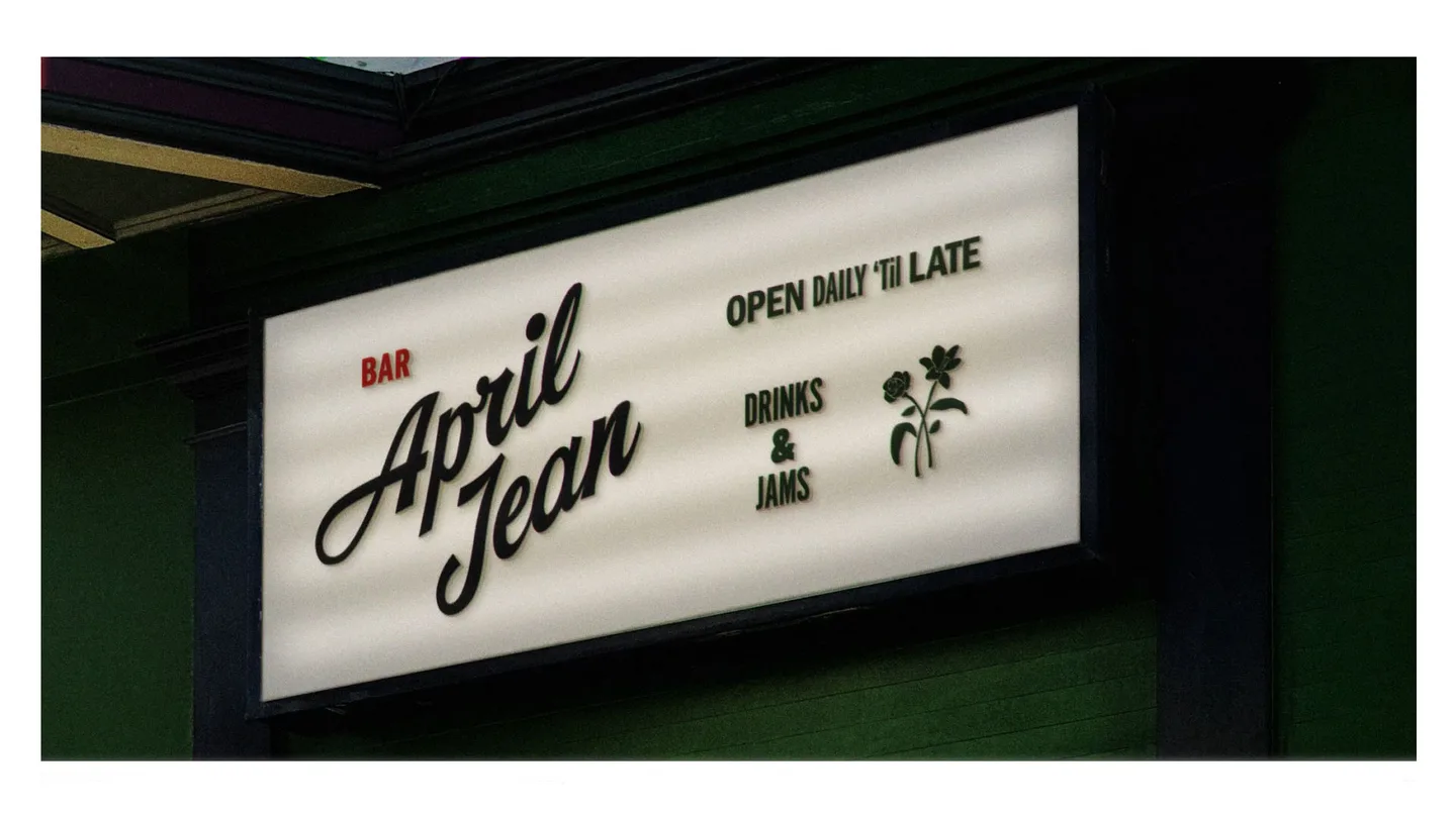 Illuminated sign reading April Jean, Open daily 'til late, Drinks and Jams, with a small flower mark.