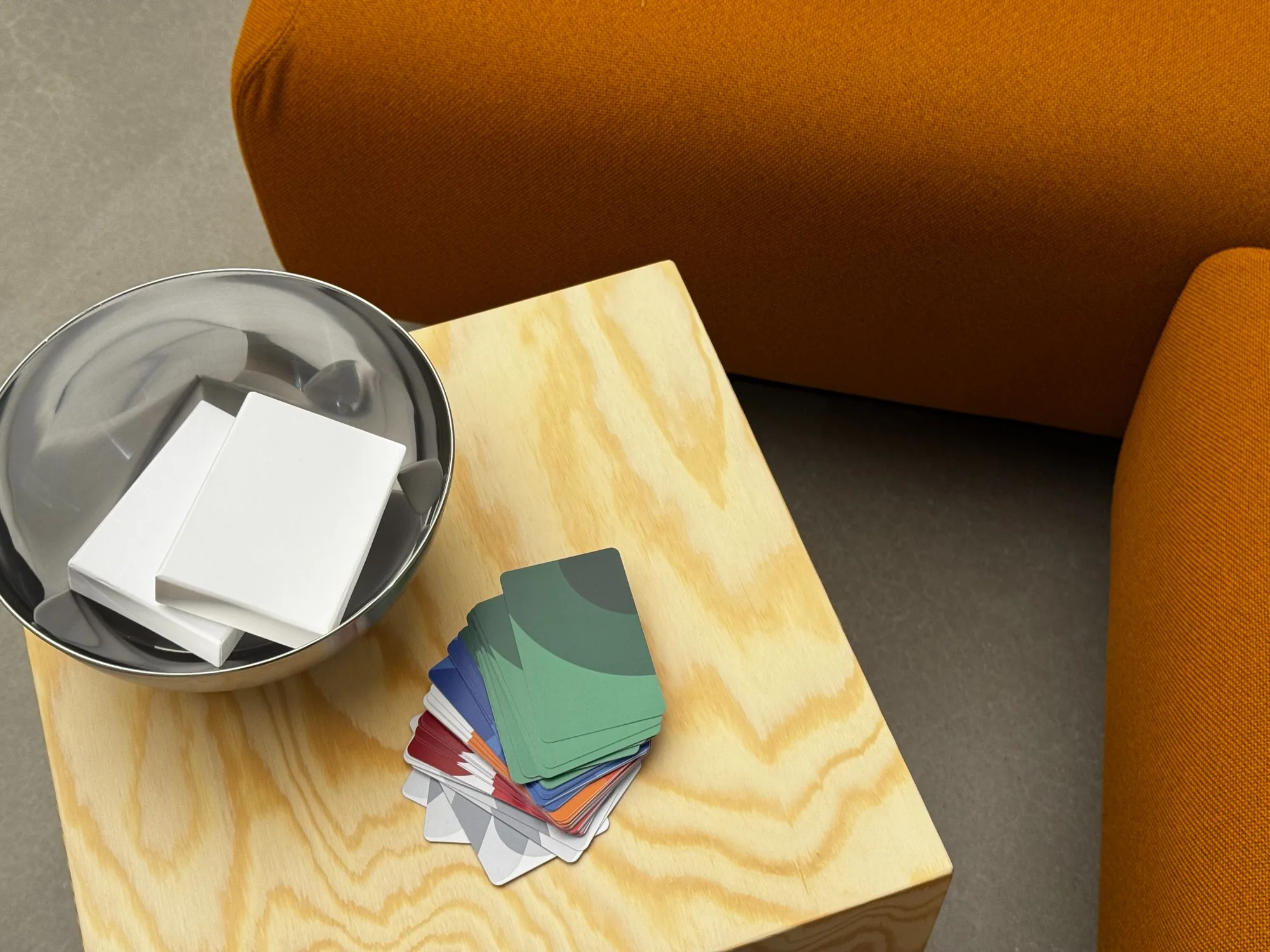 A stack of multicolored prompt cards on a timber side table beside orange seating.