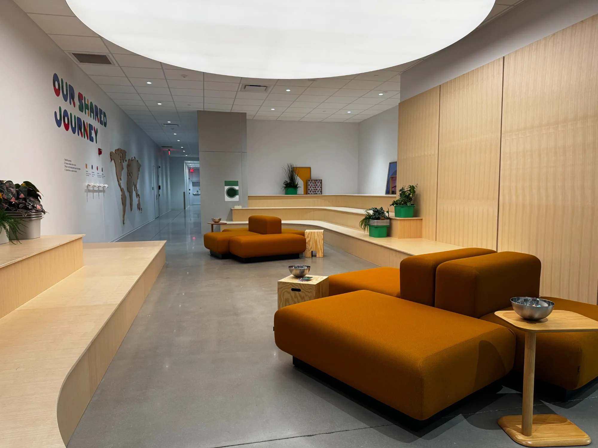 Orange modular seating and pale timber benches beneath a circular ceiling light in the GSO University gathering space.