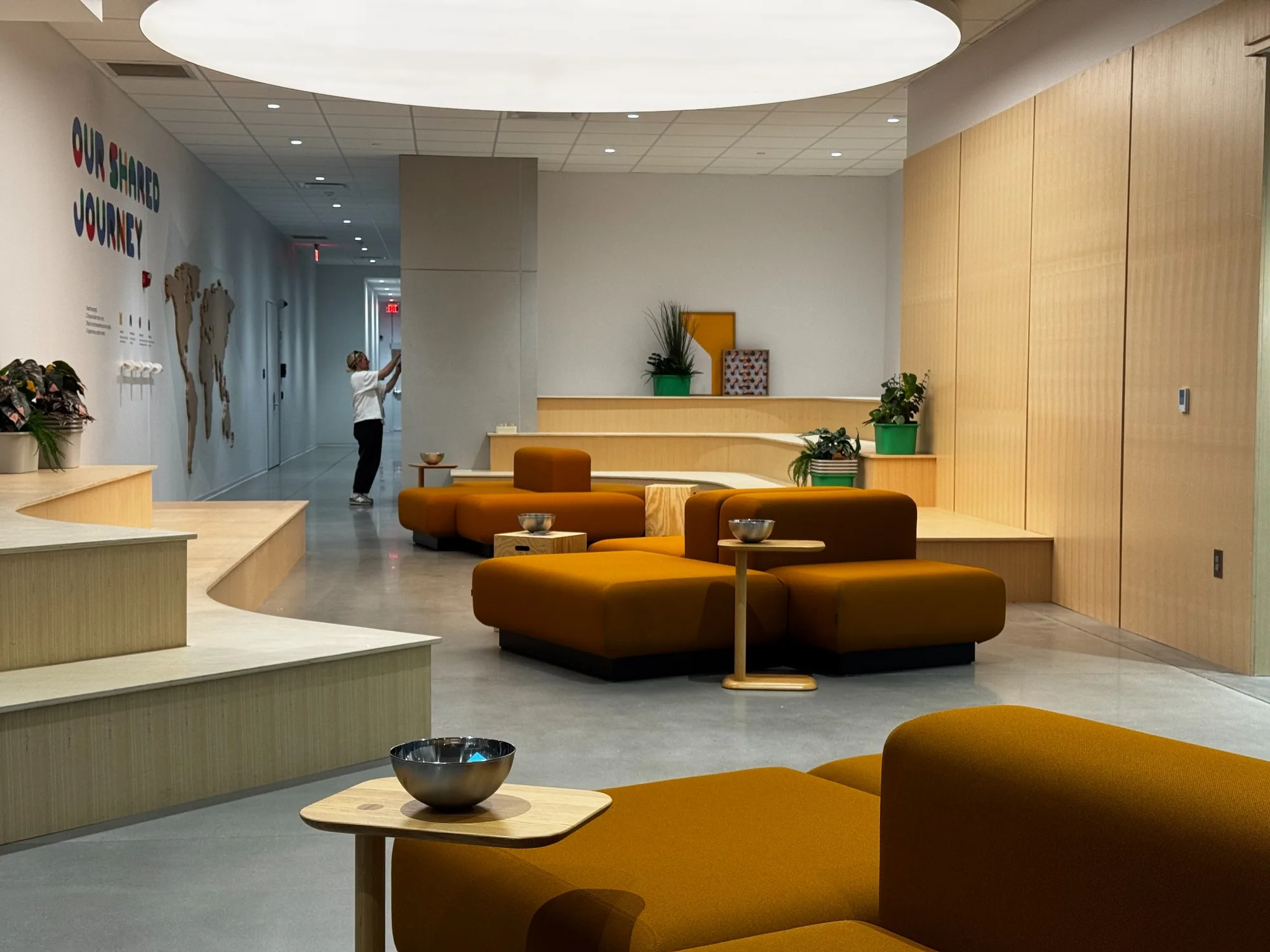 Tiered timber benches and orange lounge seating, with a person standing in the corridor beyond.