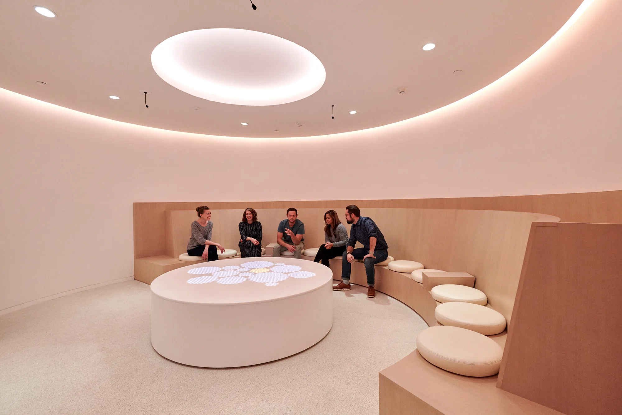 A circular room with a white round table and a curved cushioned bench beneath a ceiling oculus.