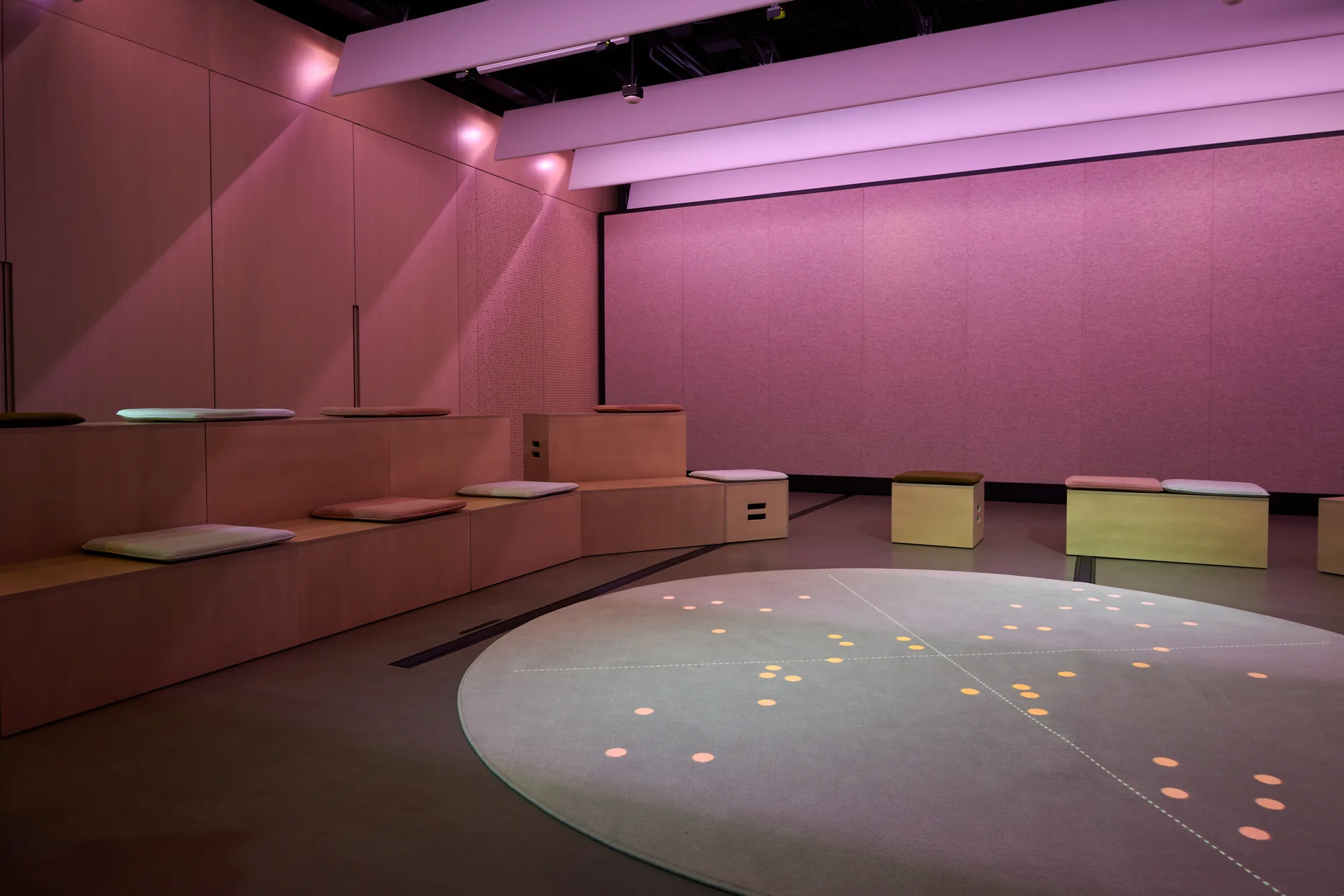A pink-lit room with tiered seating around a circular floor projection.