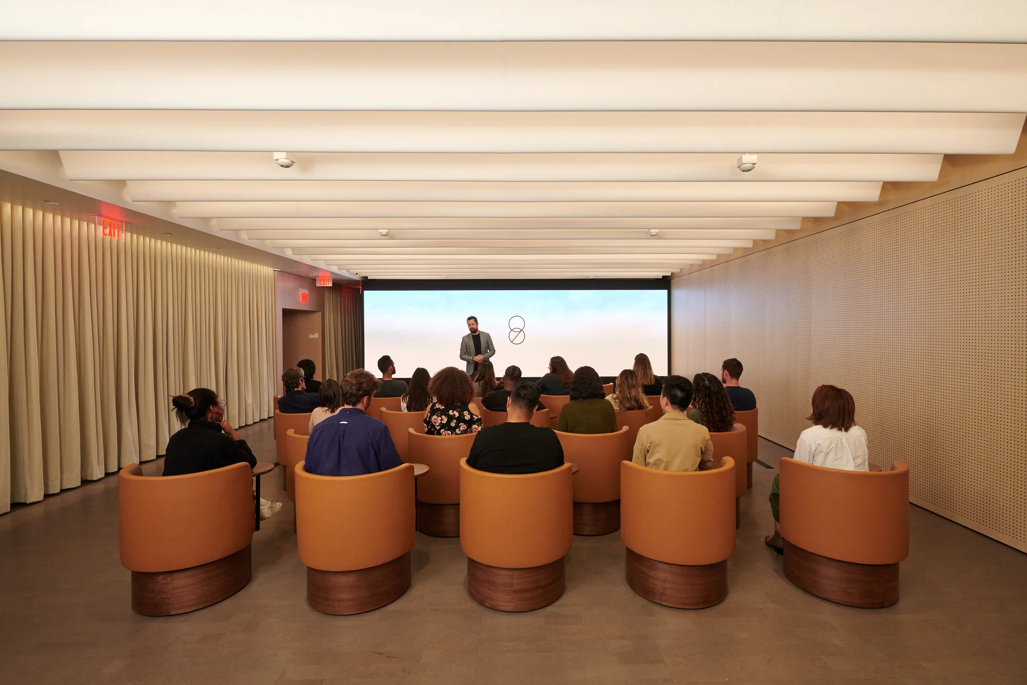 Guests seated in tan swivel chairs facing a presenter and screen.