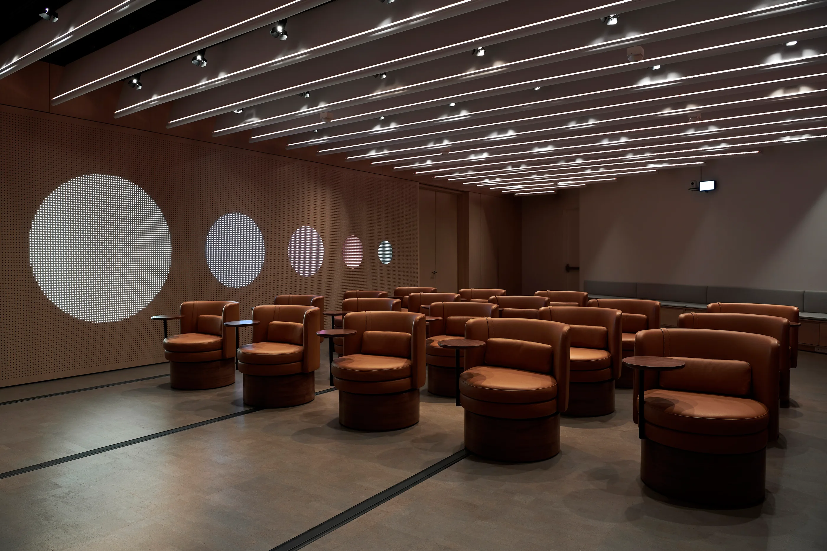 Circles of projected light on a dark timber wall above rows of seating.