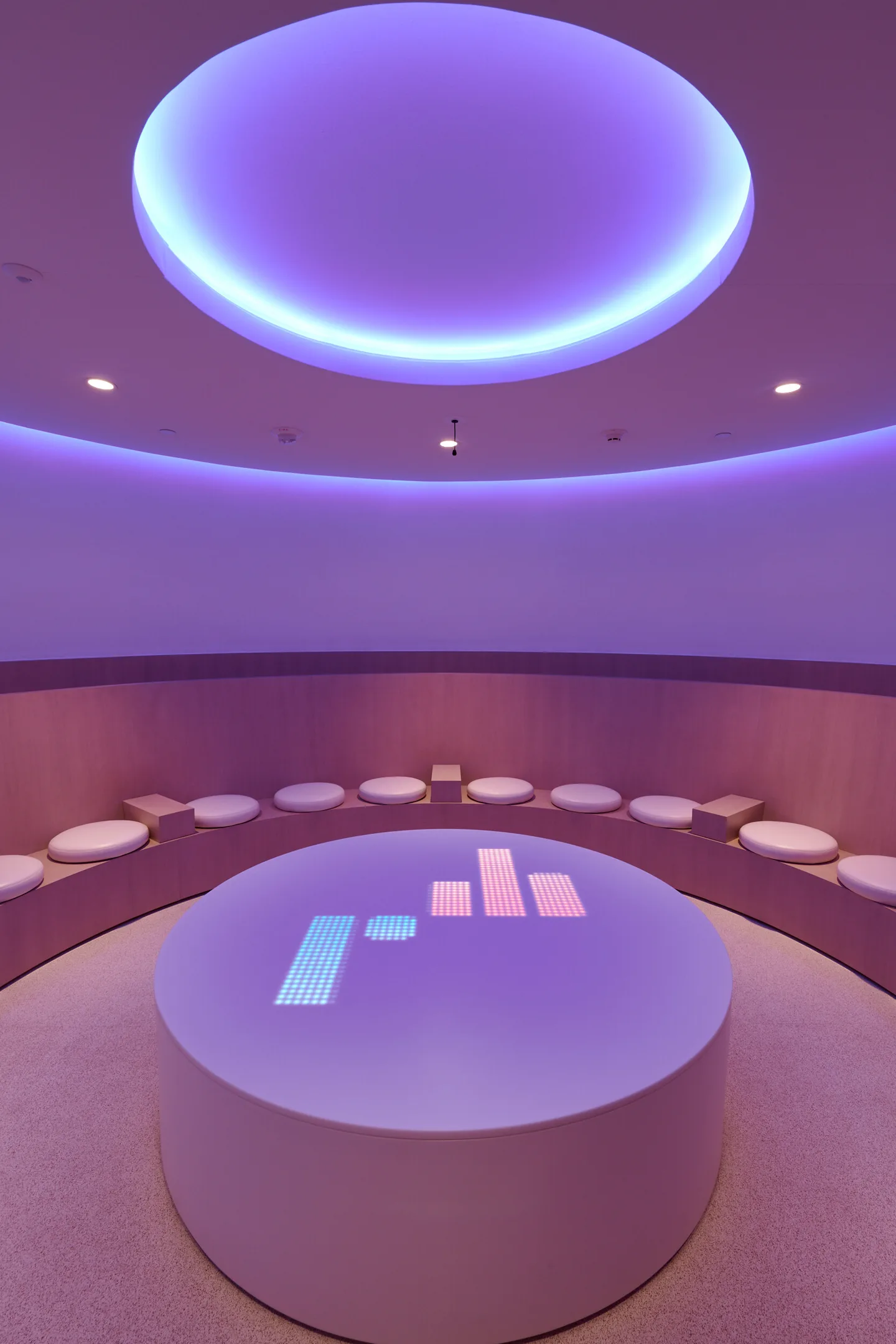 A table lit violet with a bar chart on its surface beneath a glowing ceiling ring.