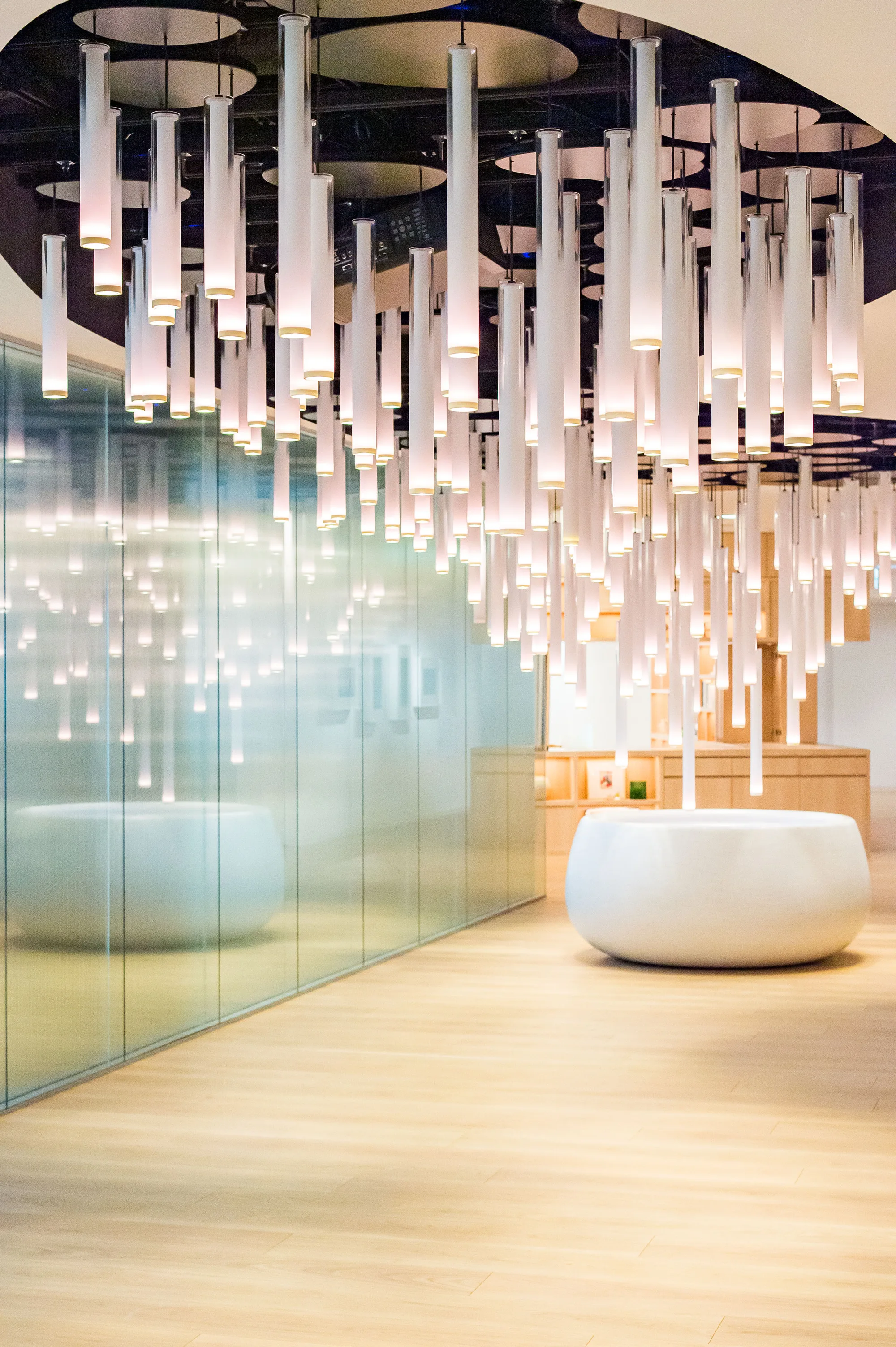 Lobby with dozens of suspended white tubes above a round white basin, with a person entering.