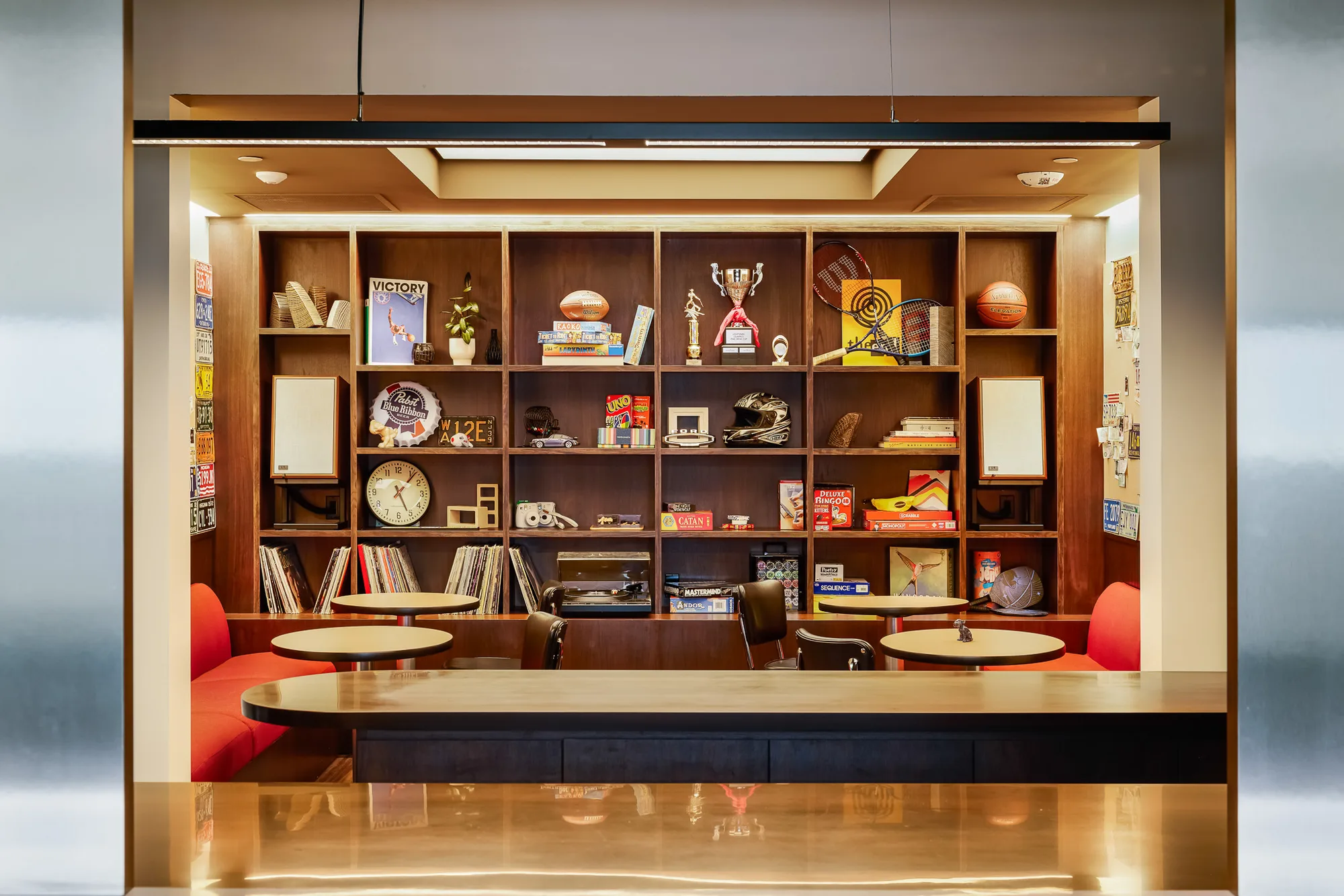 A lit timber alcove of shelves holding books, trophies, and objects above a counter with red banquette seats.