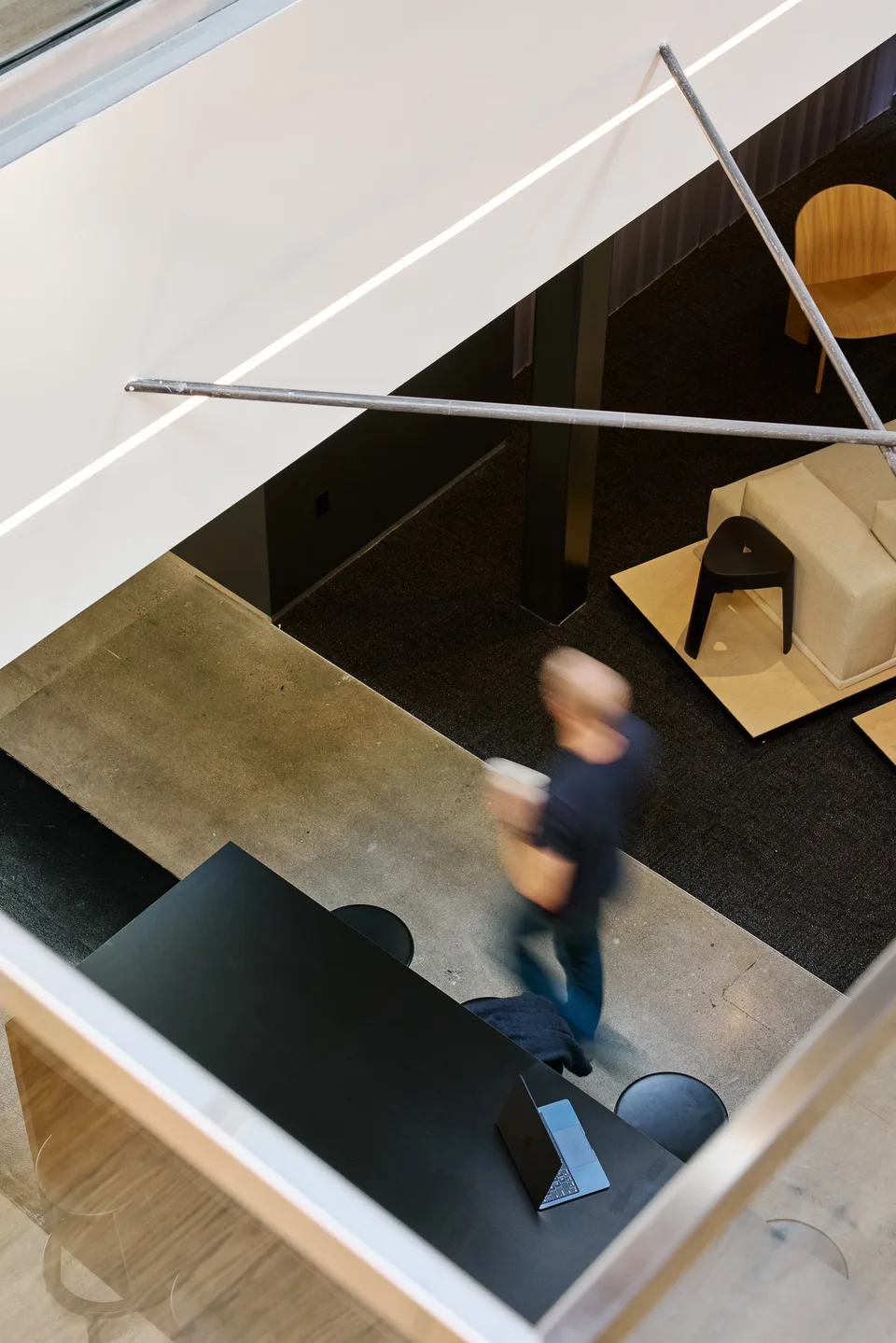 Overhead view of a person carrying a coffee past a black table and a lounge chair.
