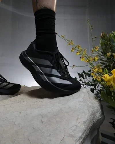 A black running shoe and sock on a pale stone with yellow flowers at the side.