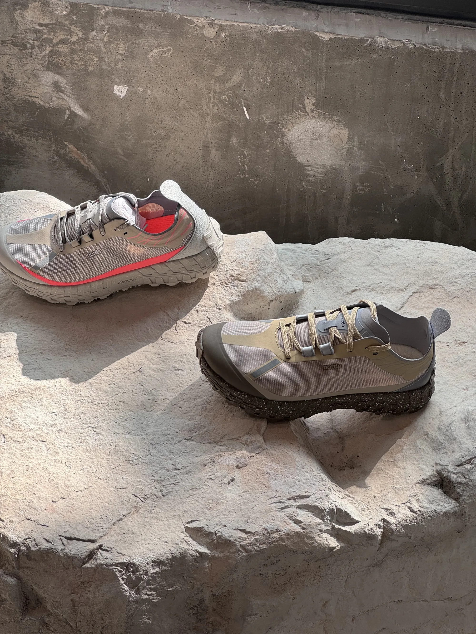 Two light trail running shoes on a rough pale boulder against a concrete wall.