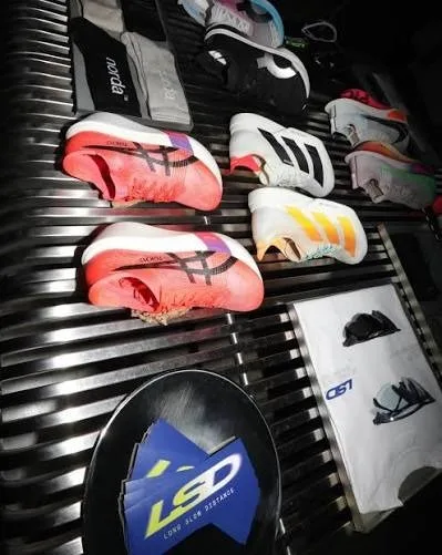Overhead view of colorful running shoes on a dark slatted surface with an LSD logo card.