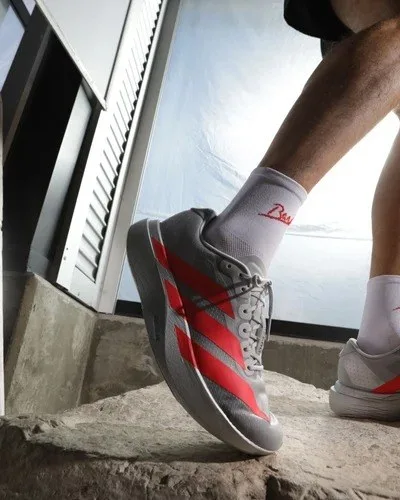 Close view of a runner's legs and red-and-white running shoes stepping onto a pale stone, with a louvered metal panel behind.