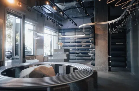 Rendered store interior with a large circular tube bench and a boulder, ceiling rail curving above.