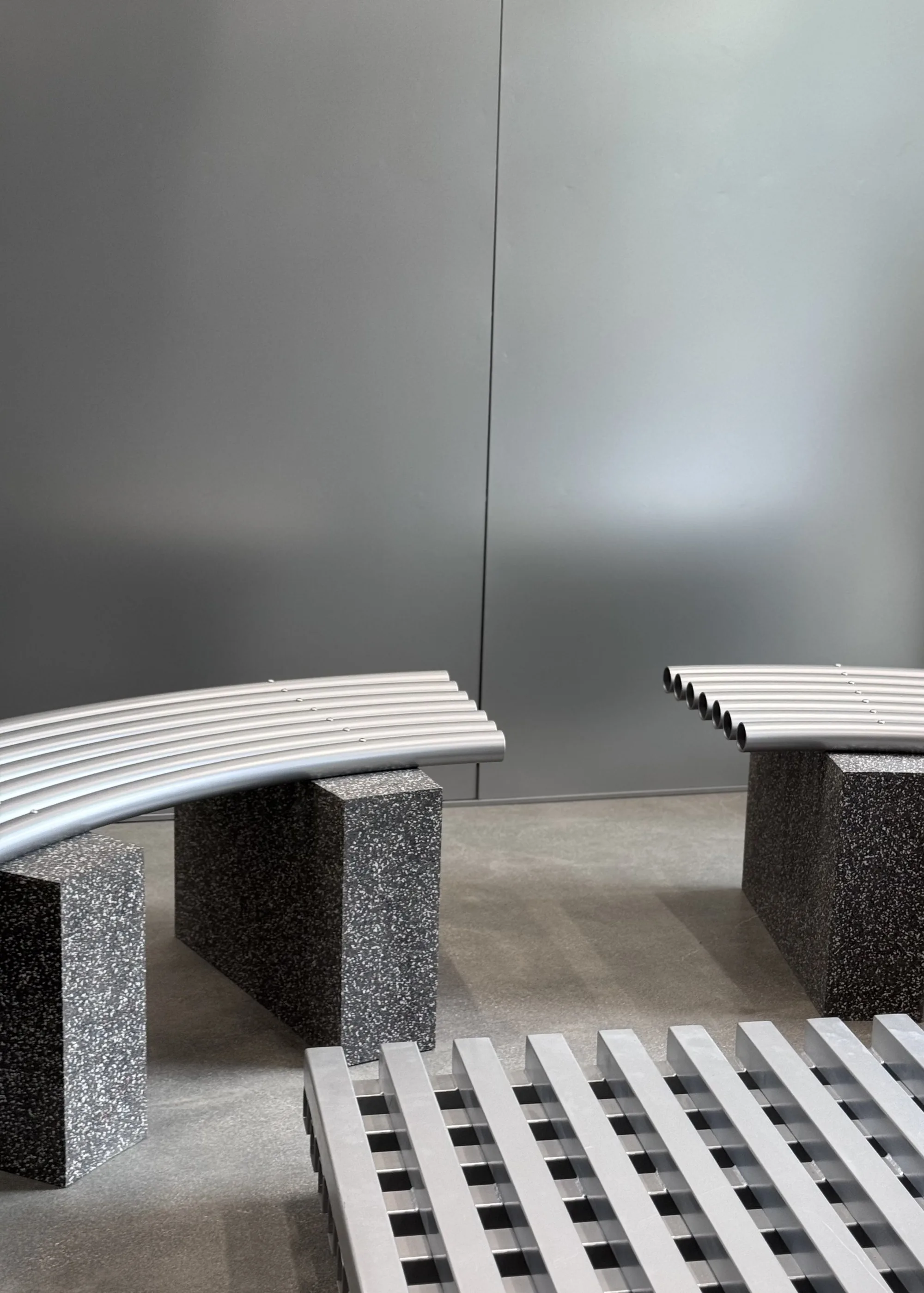 Two curved tube benches on stone blocks with a slatted platform in the foreground.