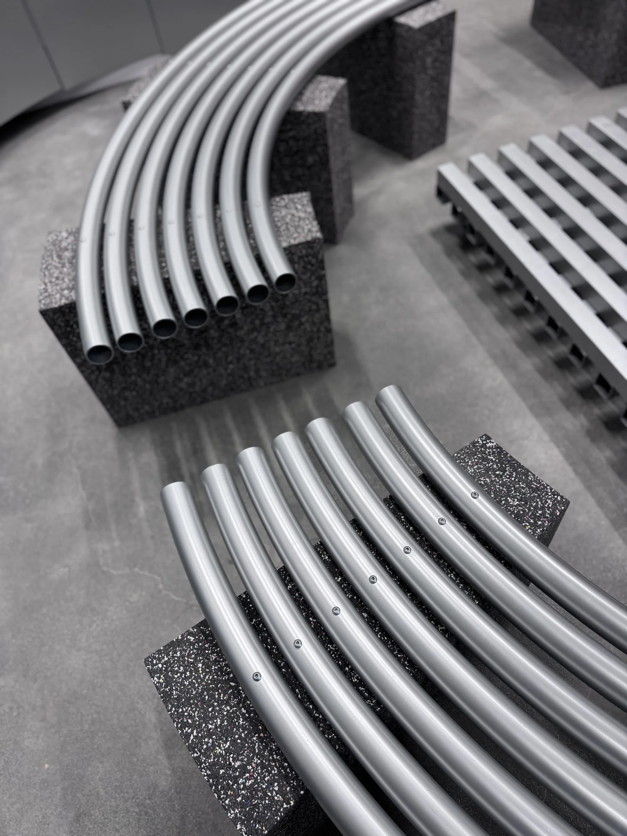 Bundled open ends of curved metal tubes on a stone block, with a slatted platform beyond.