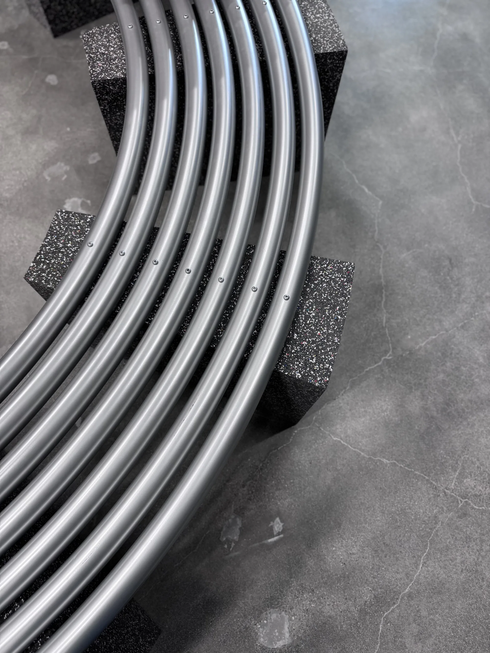 A wide arc of parallel metal tubes curving across a concrete floor.