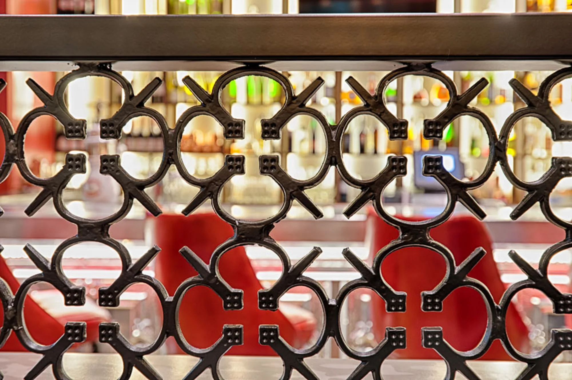 Close view of a black cast screen pattern with red bar stools blurred behind it.