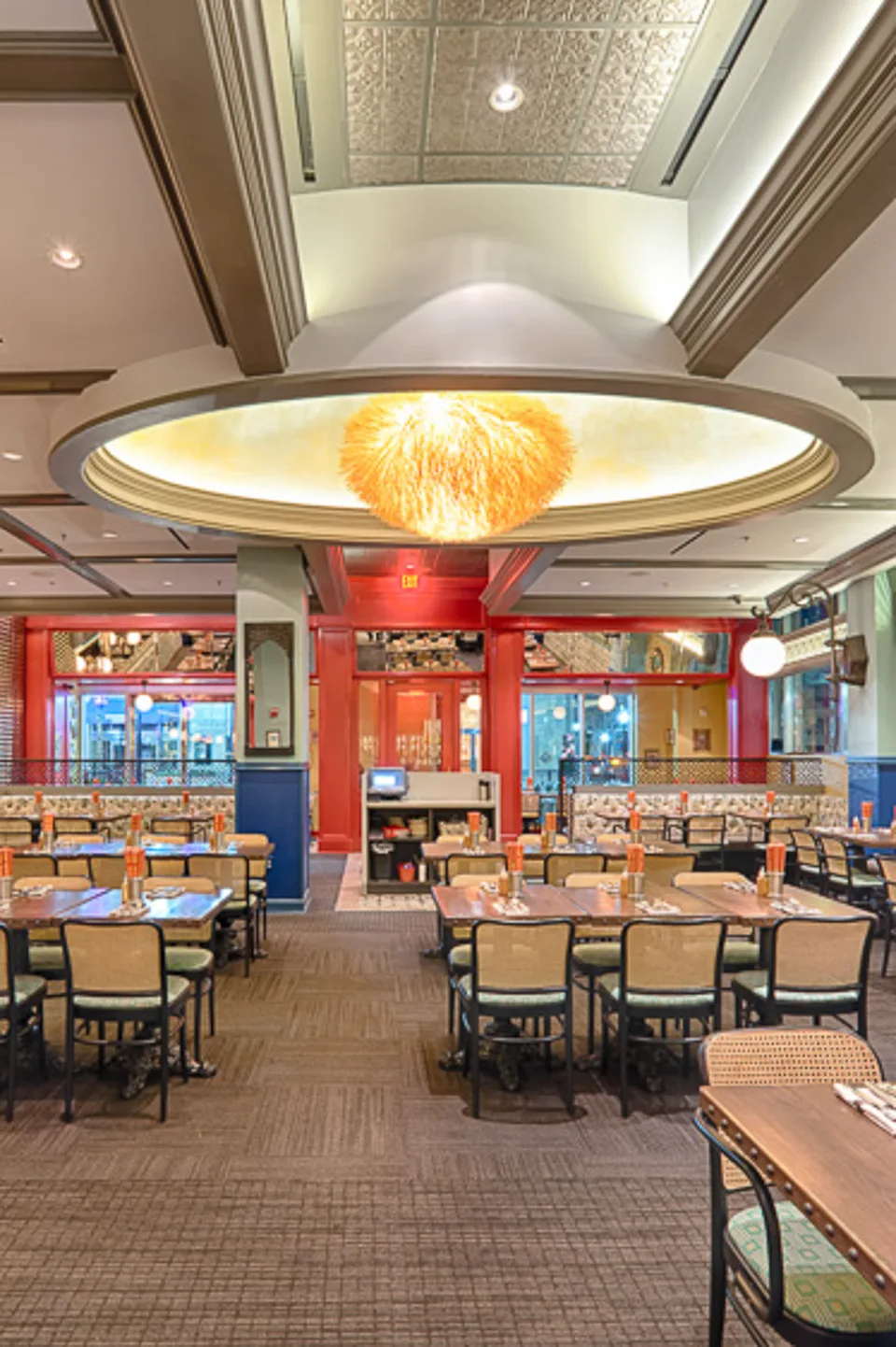 Dining room seen from the end of a table, with a glowing oval ceiling and red bar at the far end.