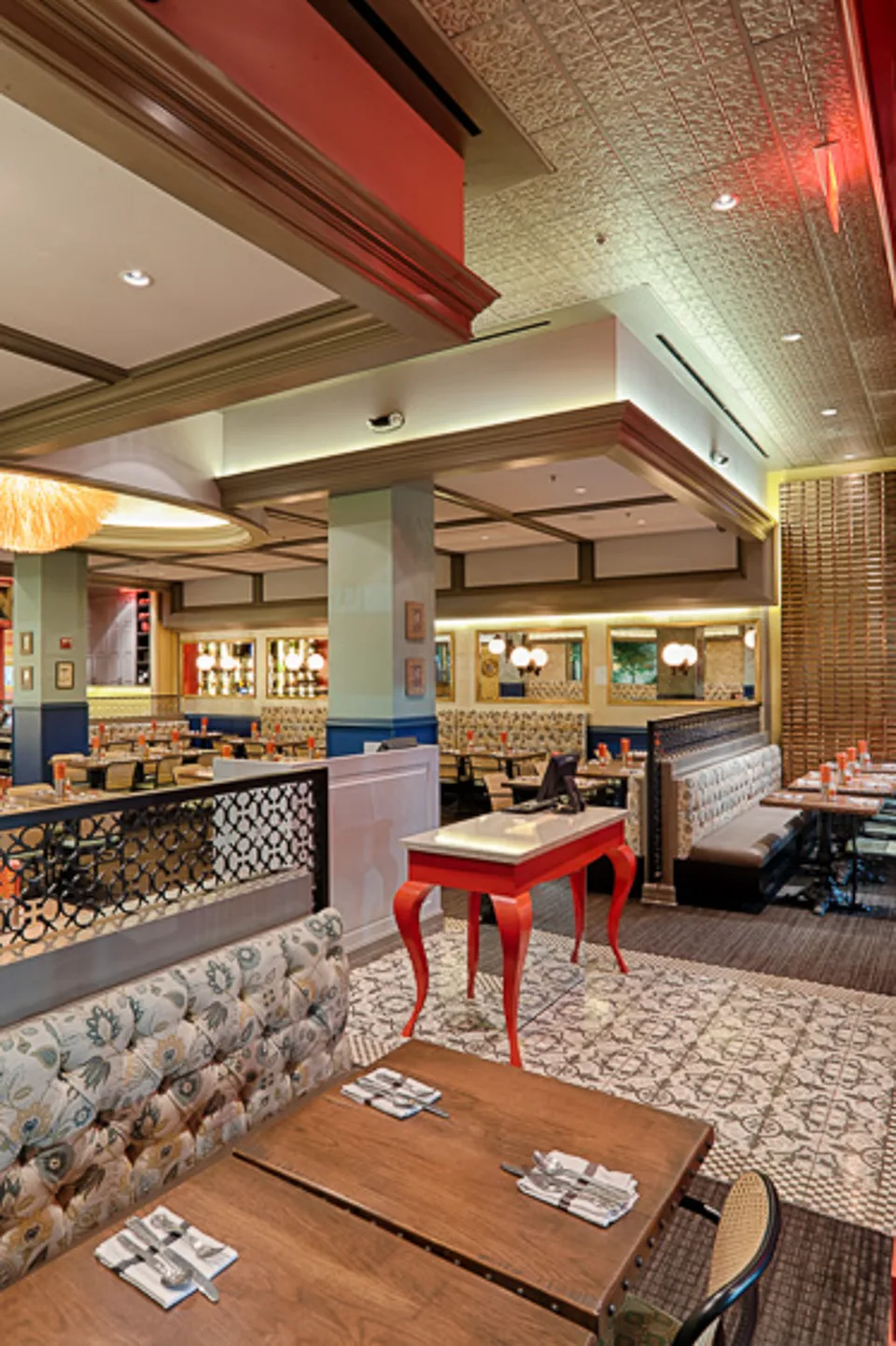 A red table with curved legs beside a patterned banquette, timber tables, and a patterned floor.