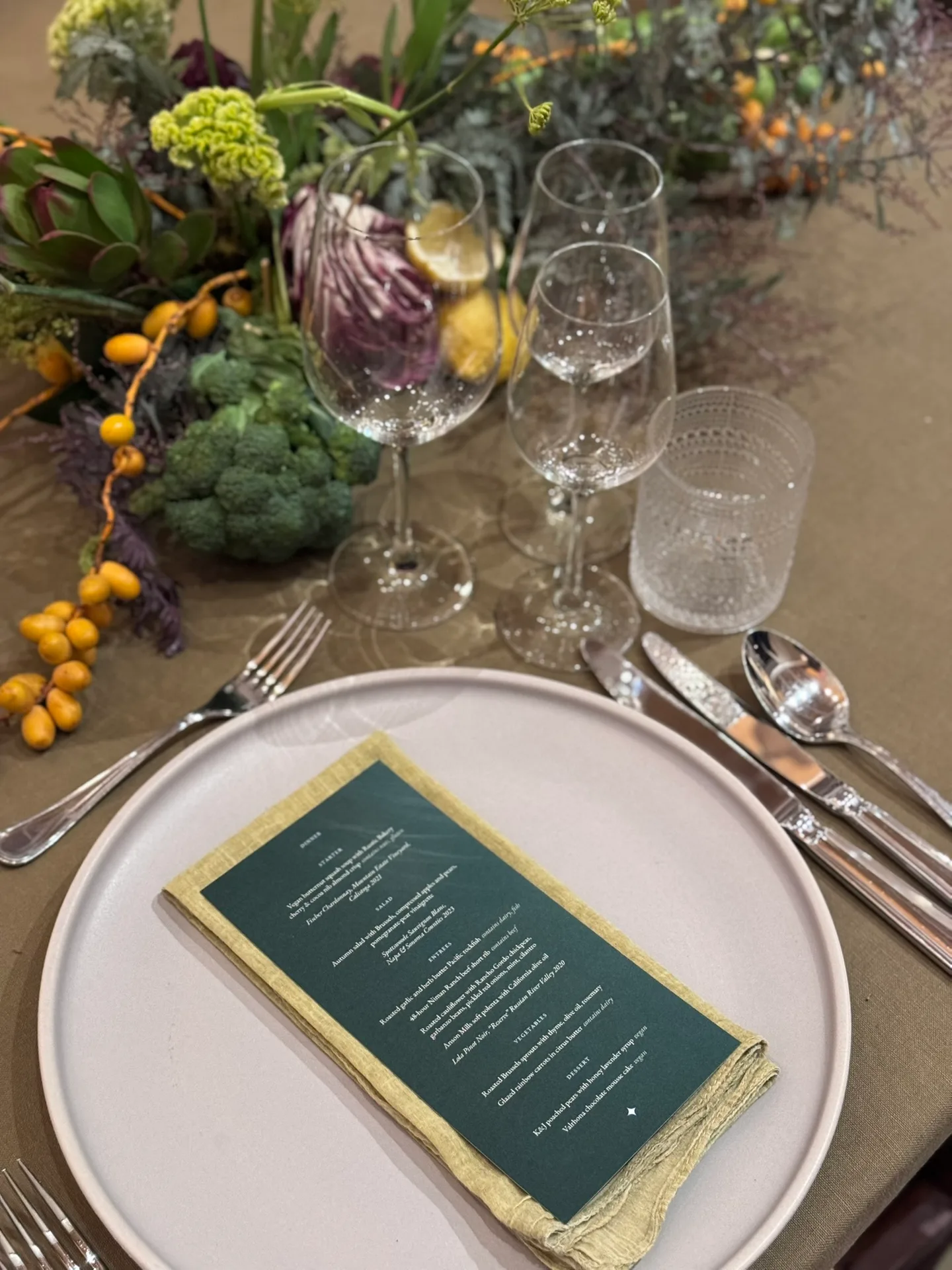 A plate with a green printed menu and cutlery, among greens, citrus, and flowers.