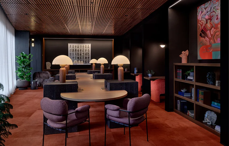 A dark library room at Bellevue with a long table, mushroom lamps and shelves.