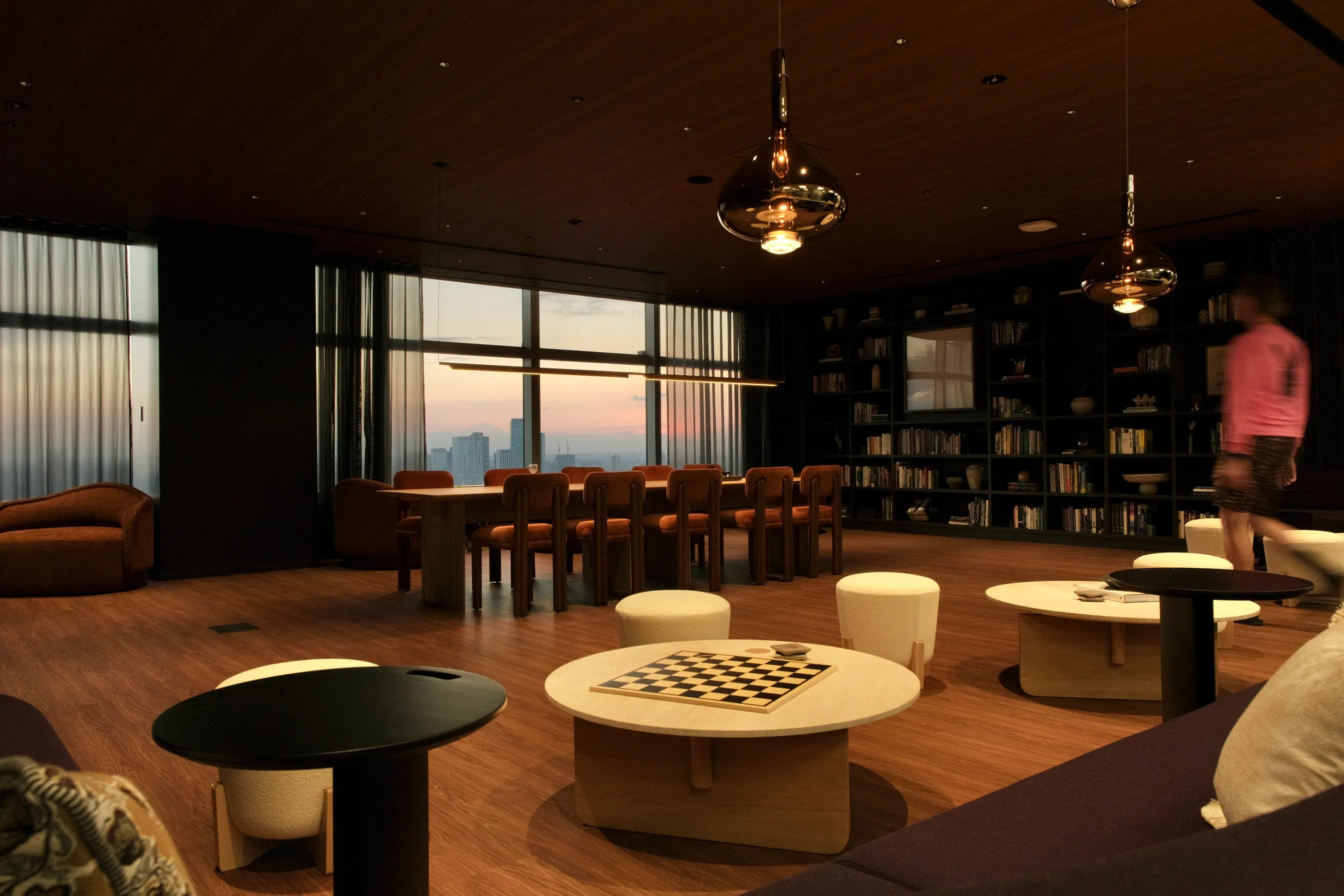 A dark library lounge with bookshelves, a long table and a chess board.