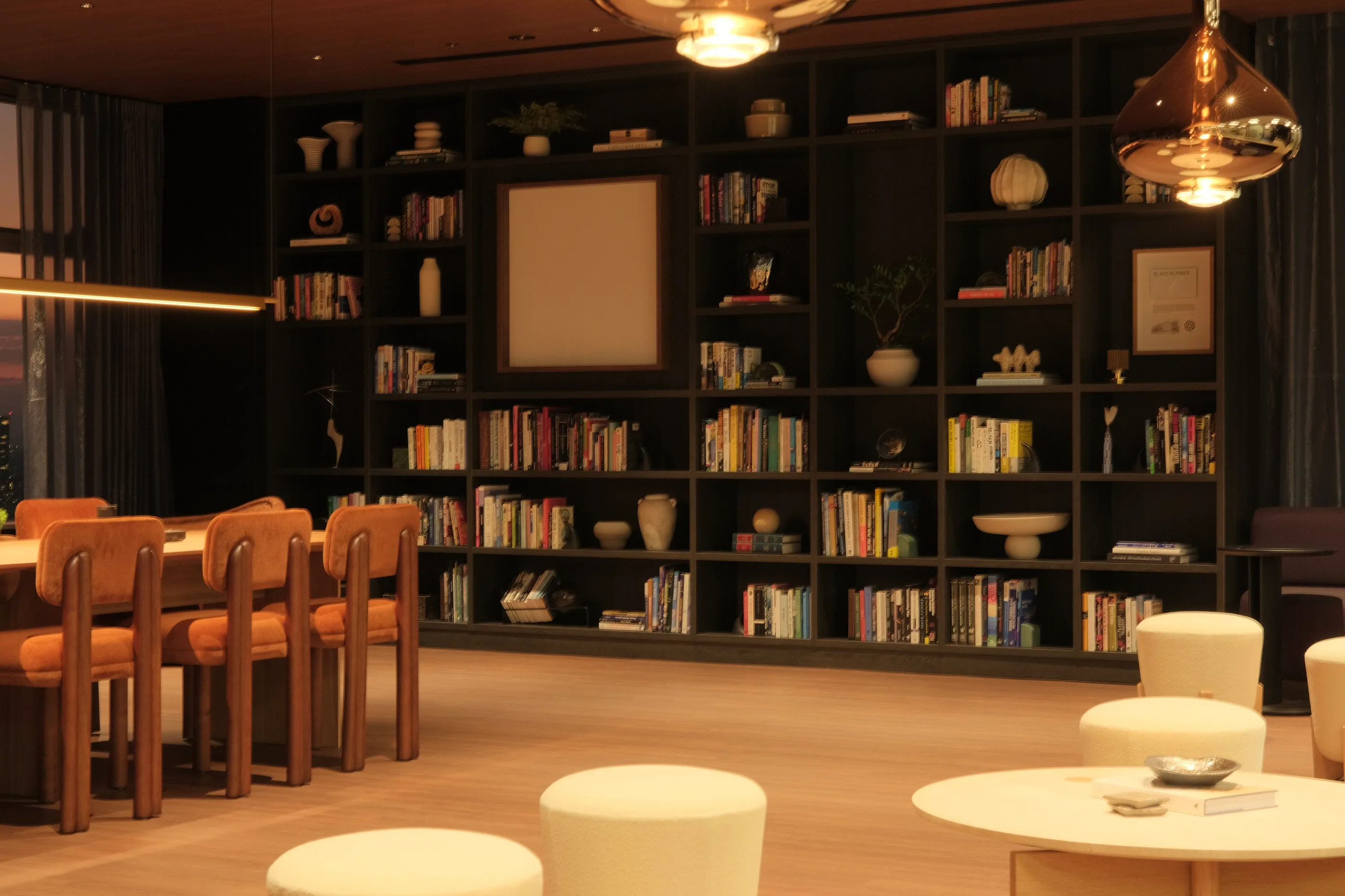 Dark shelving filled with books above a table and rust-colored chairs.