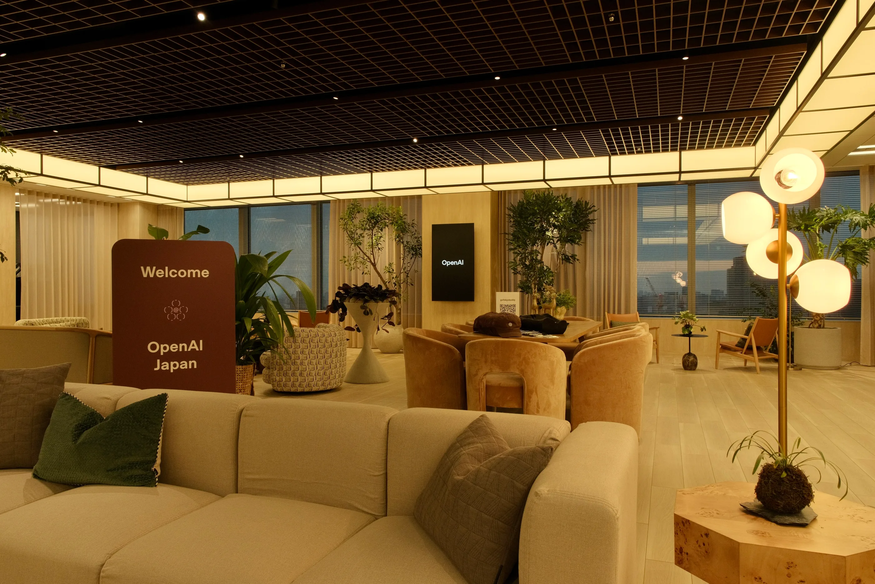 A sofa lounge with plants and a wall screen in a timber-ceilinged room.