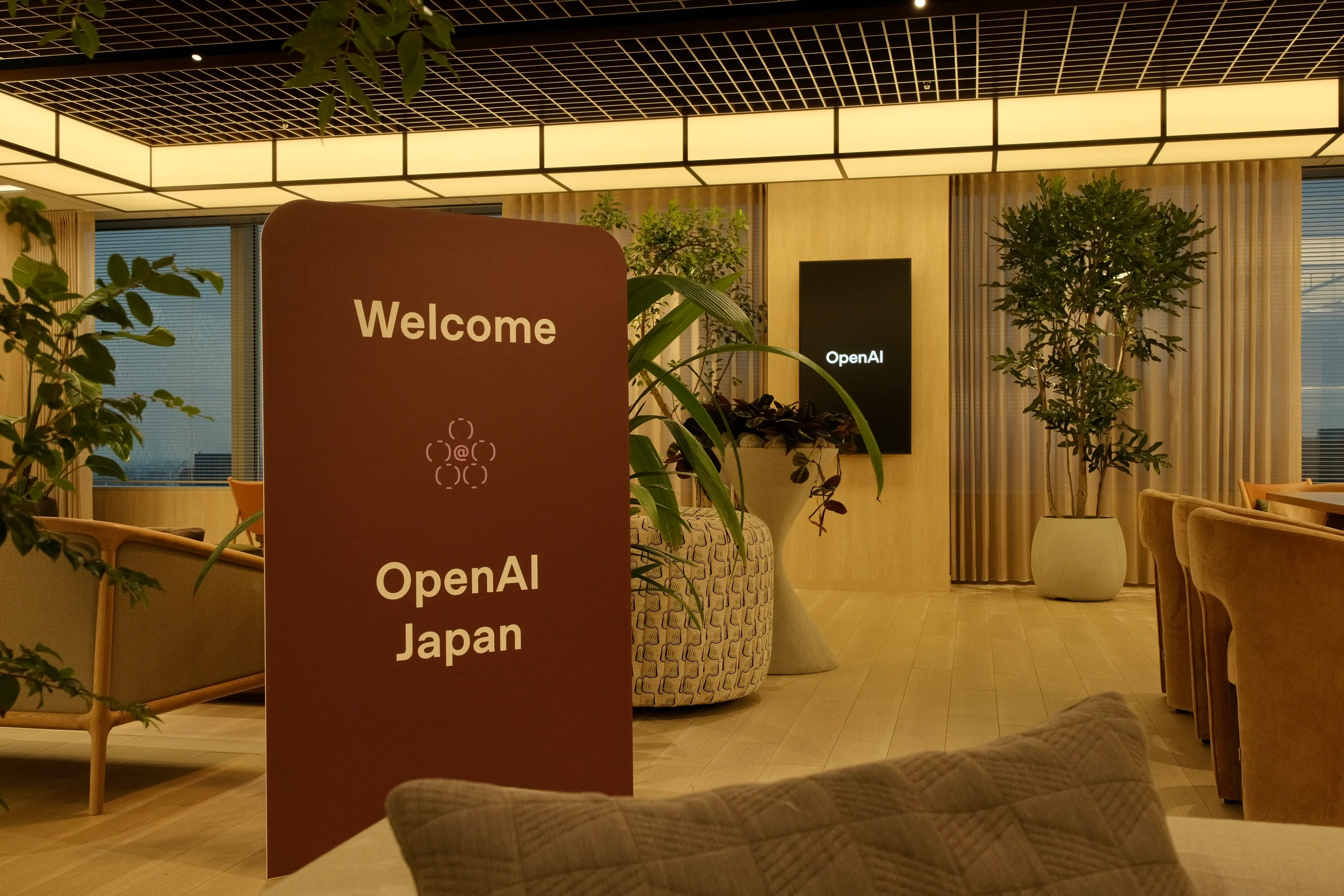 A maroon Welcome OpenAI Japan sign standing among plants and lounge seating.