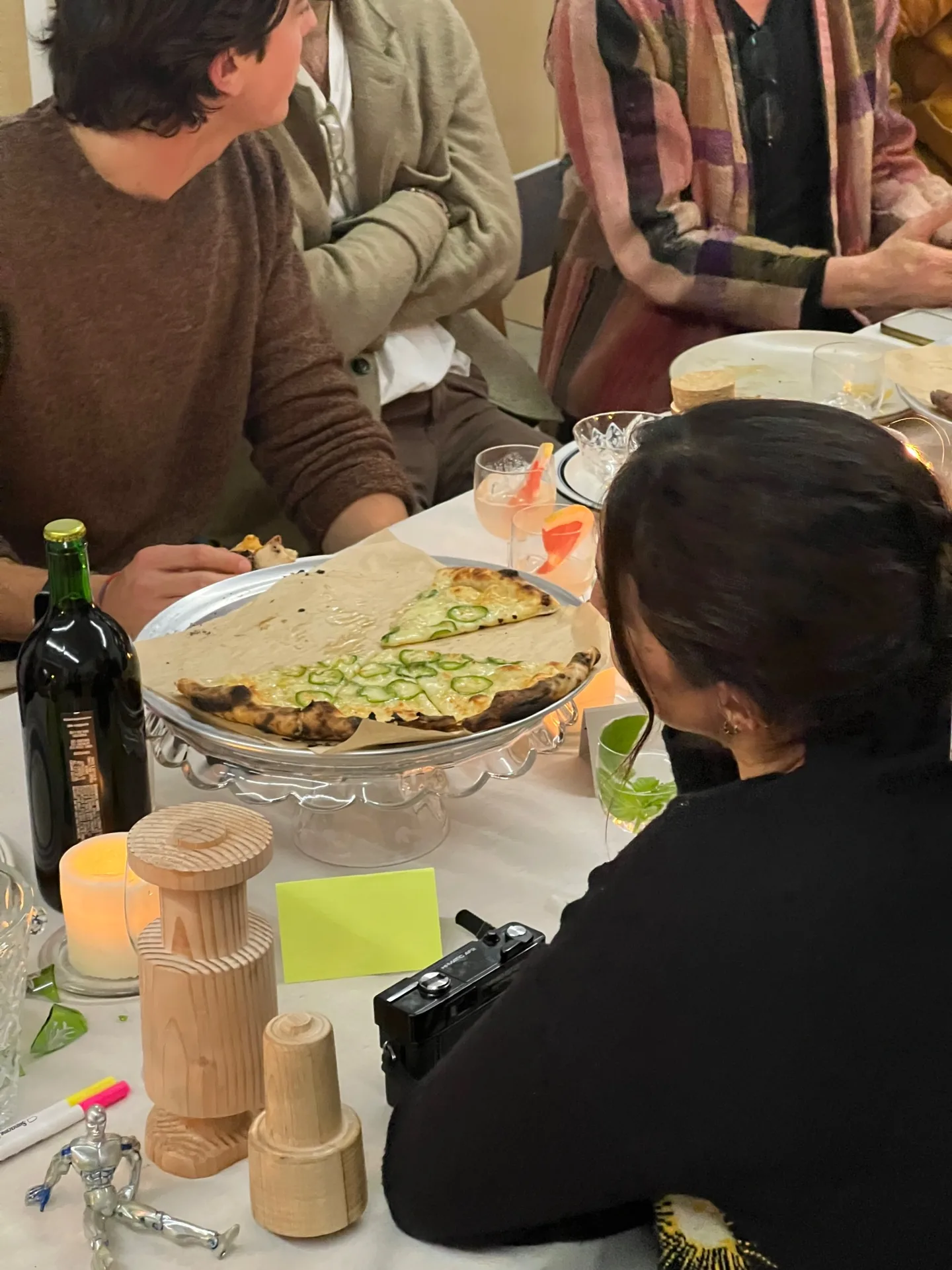 Guests seated close at a table, one person turned toward a shared dish of flatbread.