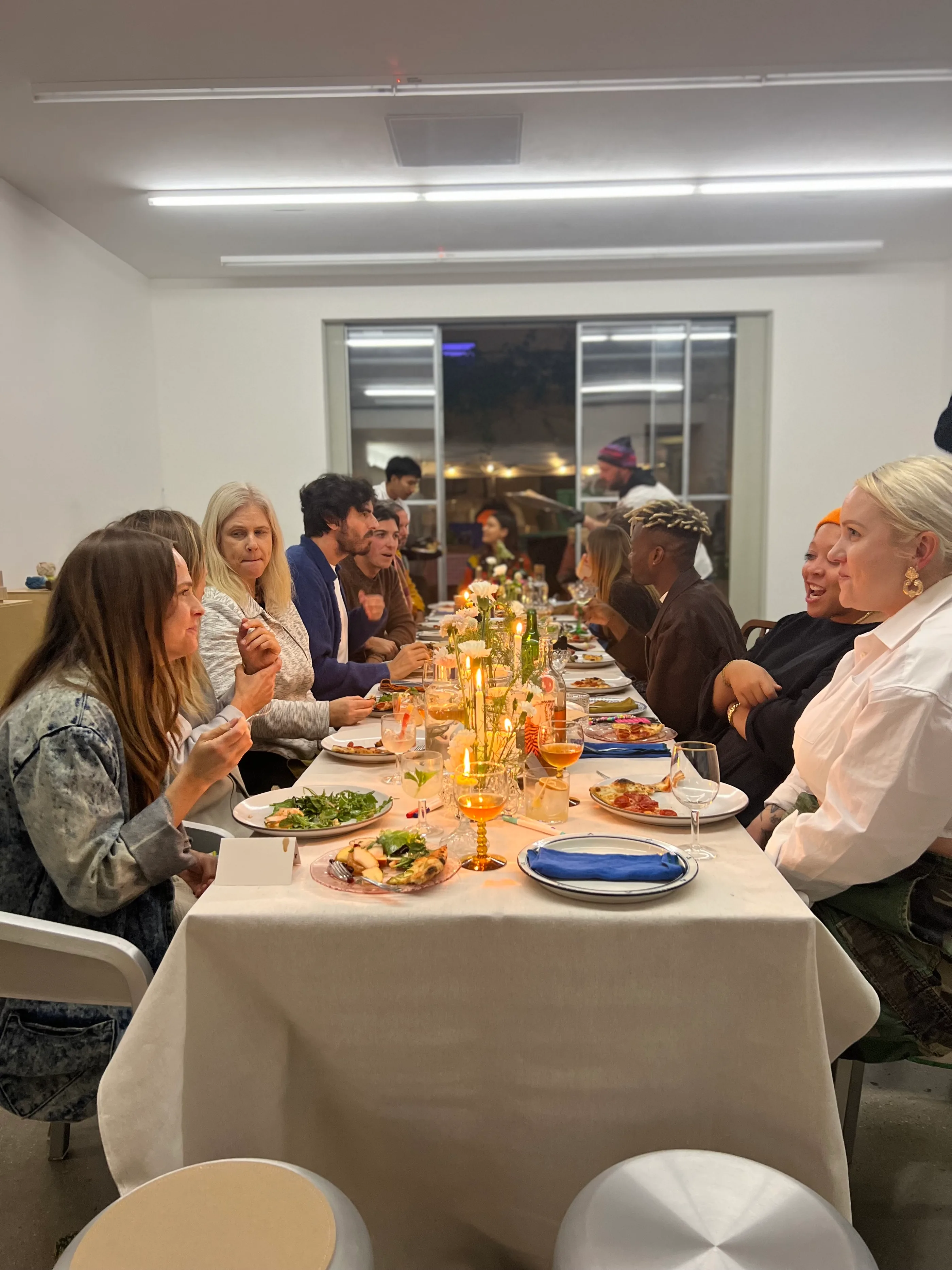 A very long table in a bright room with guests seated on both sides and candles along its length.