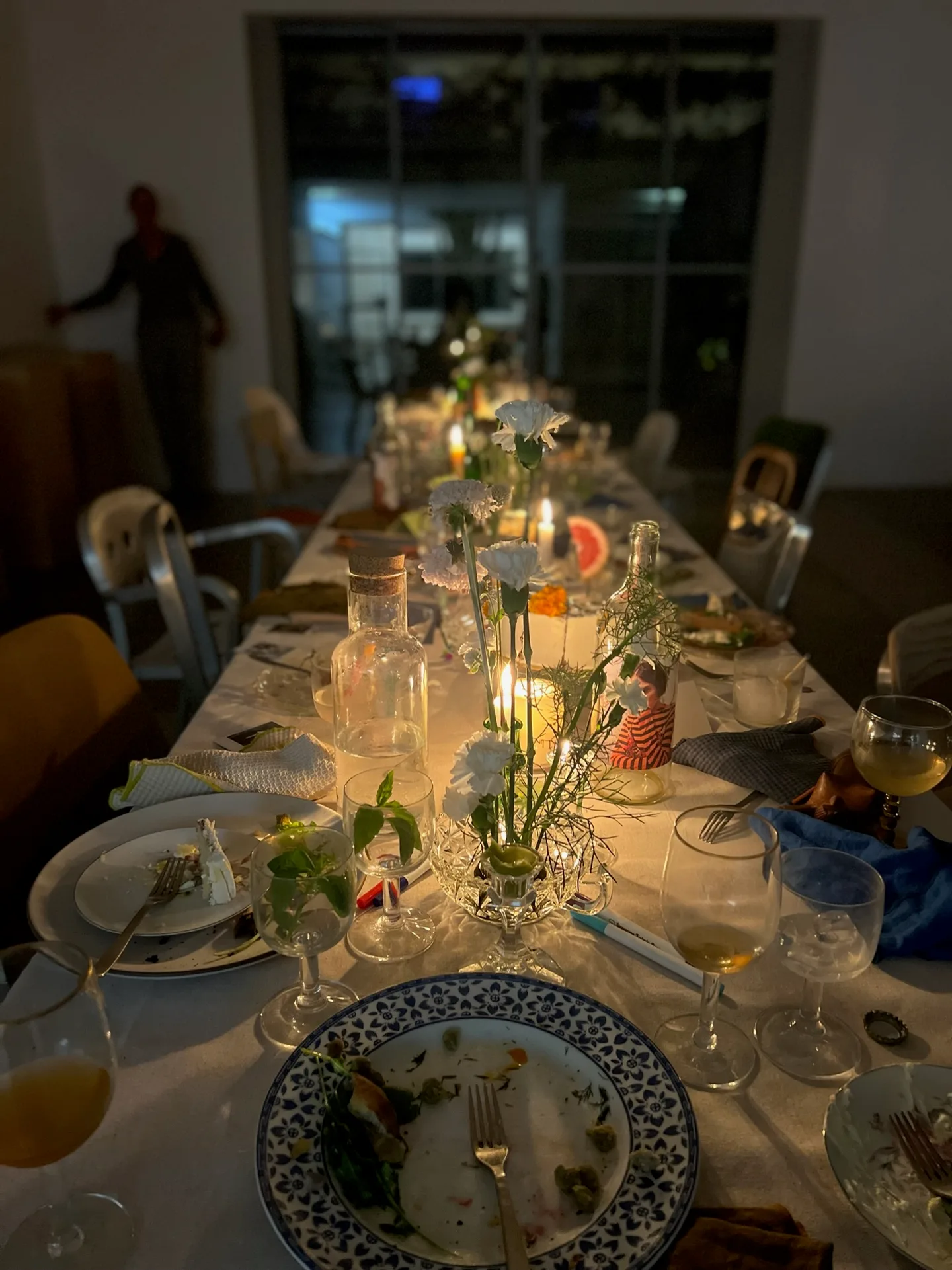 A long table lit by candles in a dim room with a large window at the far end.