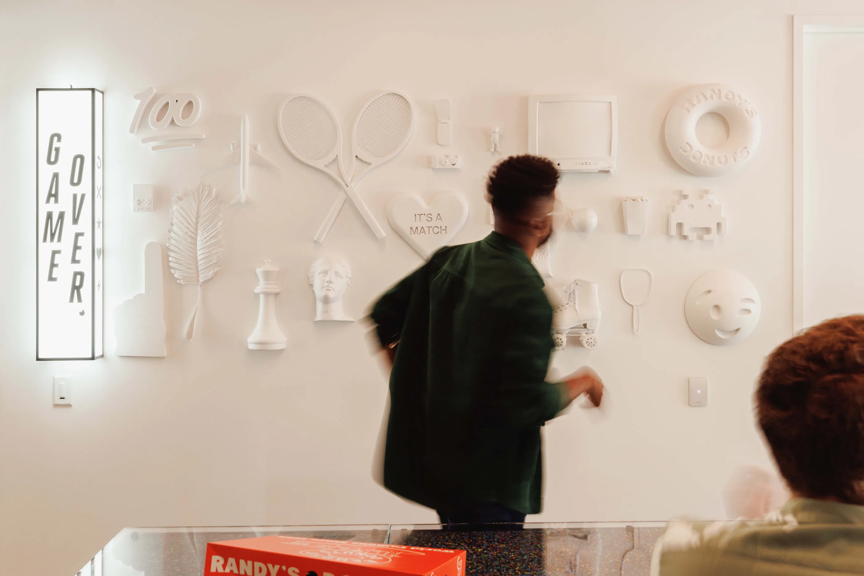 A person looking at a white wall covered in cast relief objects, with Game Over lettering beside it.