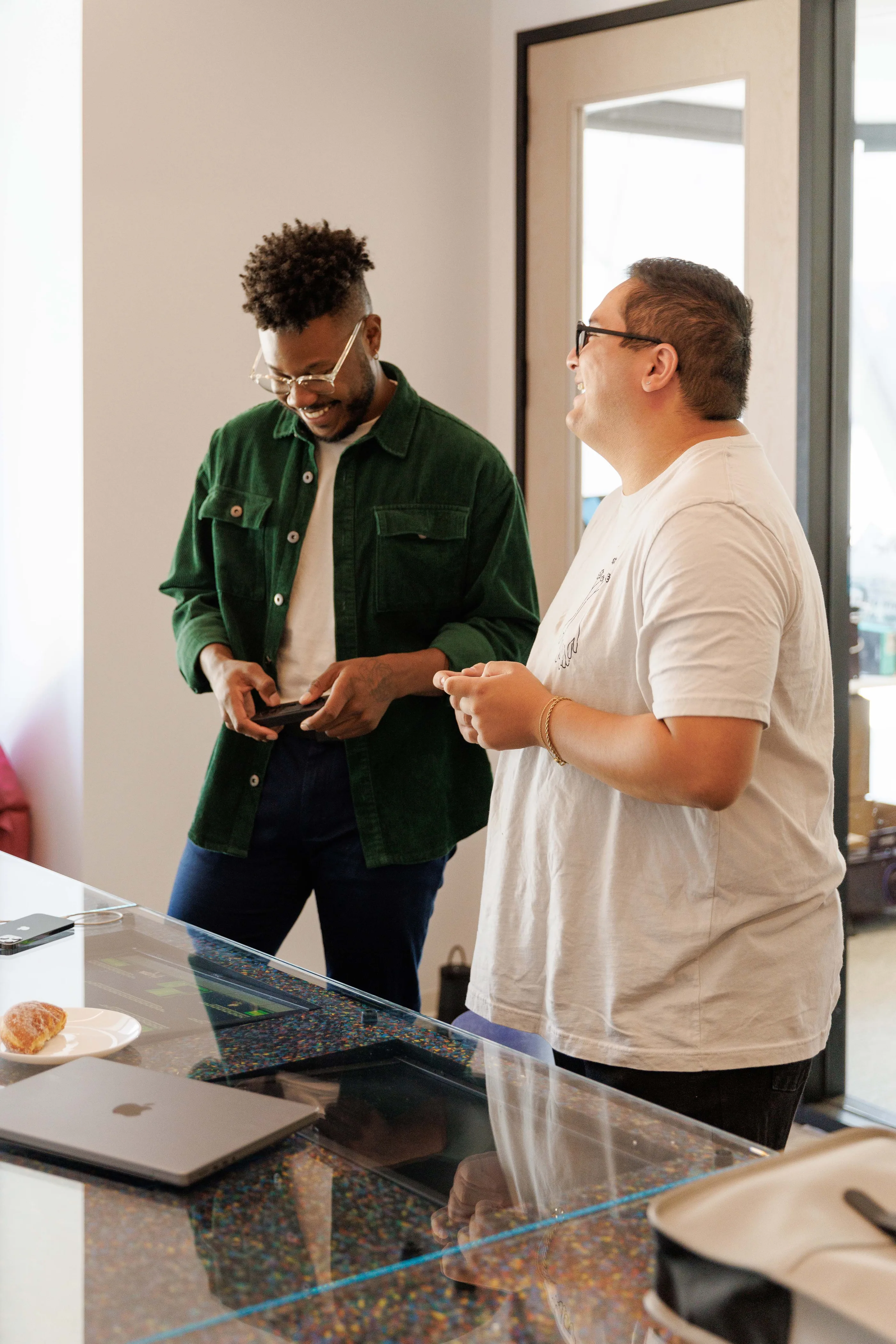 Two people talking beside a glass and terrazzo table with a laptop on it.