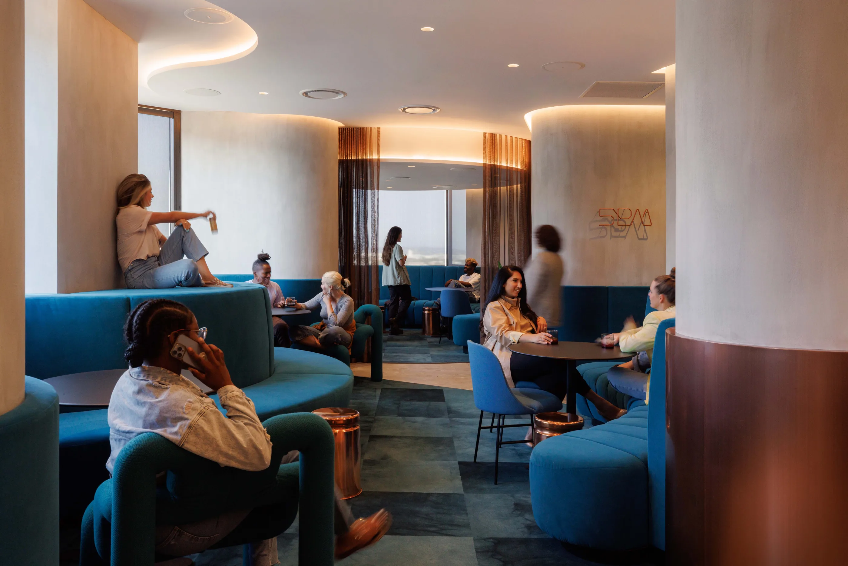 Dim lounge with blue curved banquettes, round tables, and people talking in small groups.