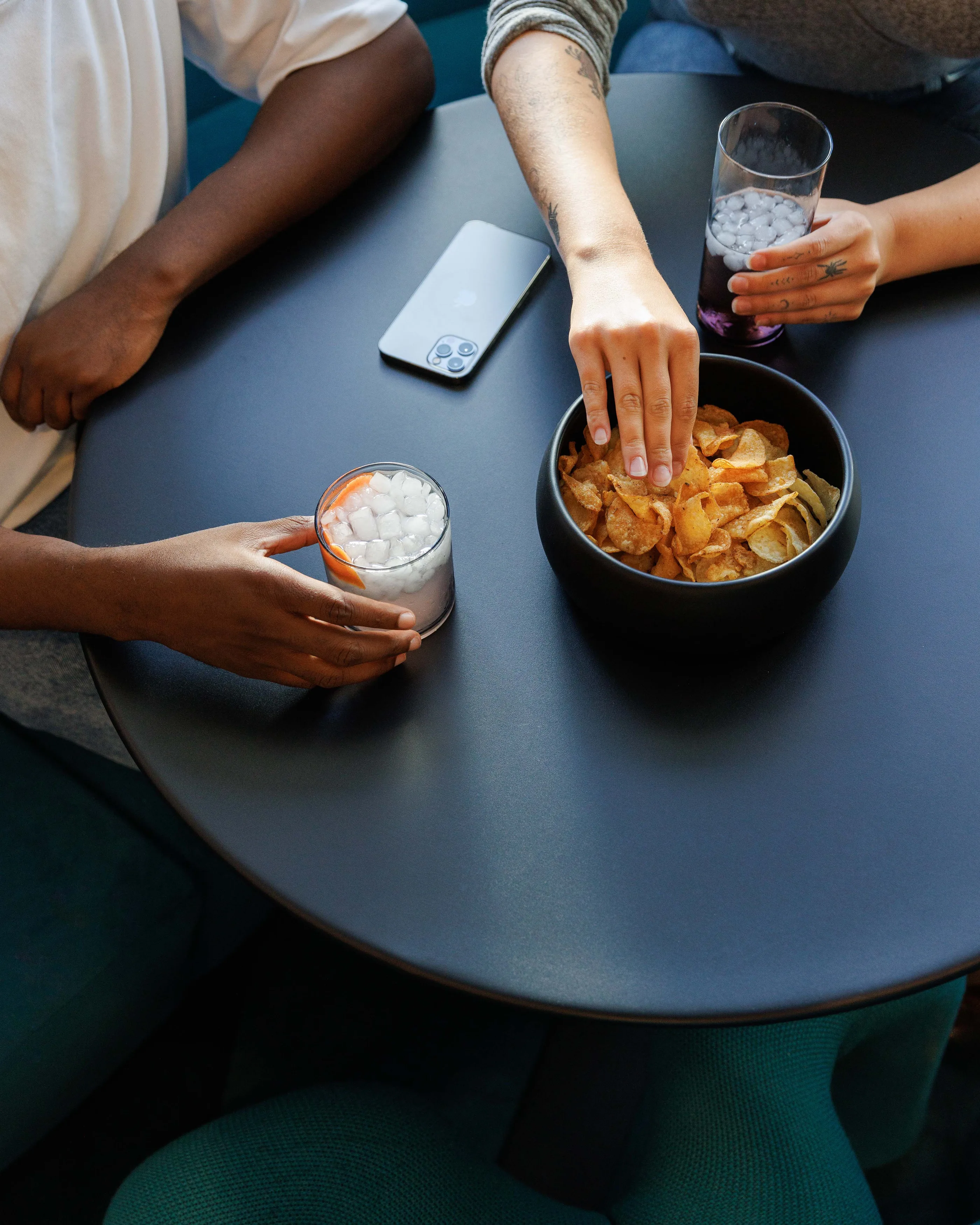 Close view of hands reaching for snacks and drinks on a dark round table.