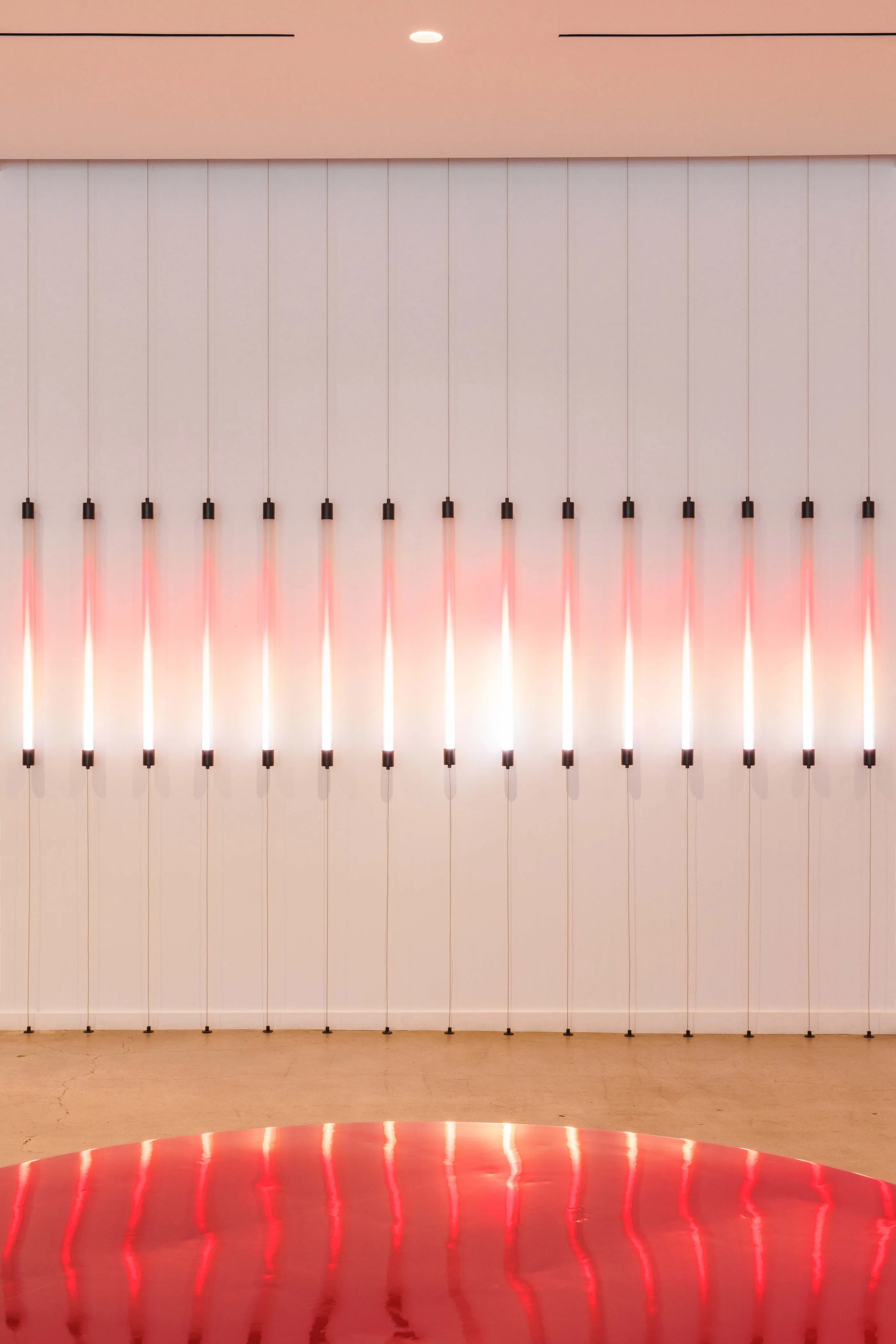 Close view of a row of vertical pink and white light tubes against a pale wall, with red upholstery below.