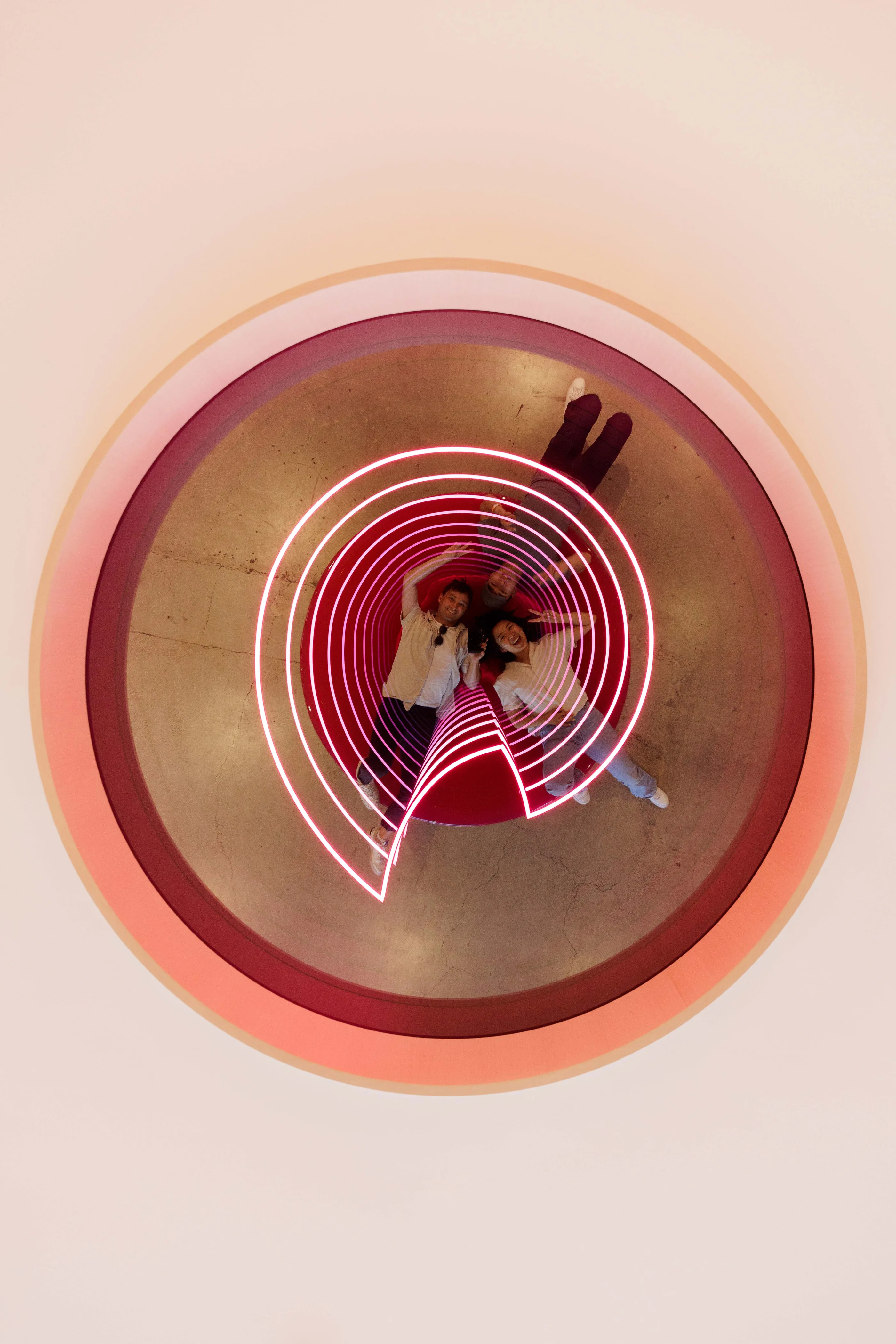 View from above of a round seat with concentric pink light rings and two people lying on it.